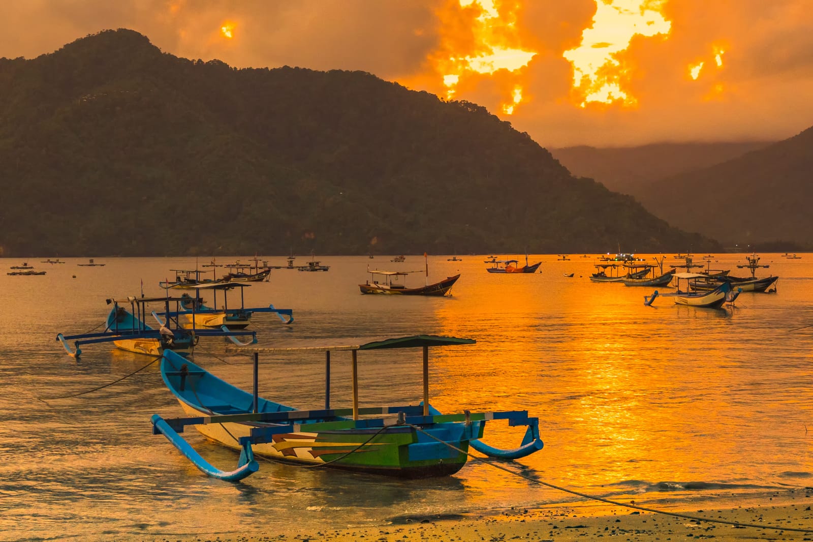 colorful boats docked on a calm lake at sunset, with mountains and clouds in the background.