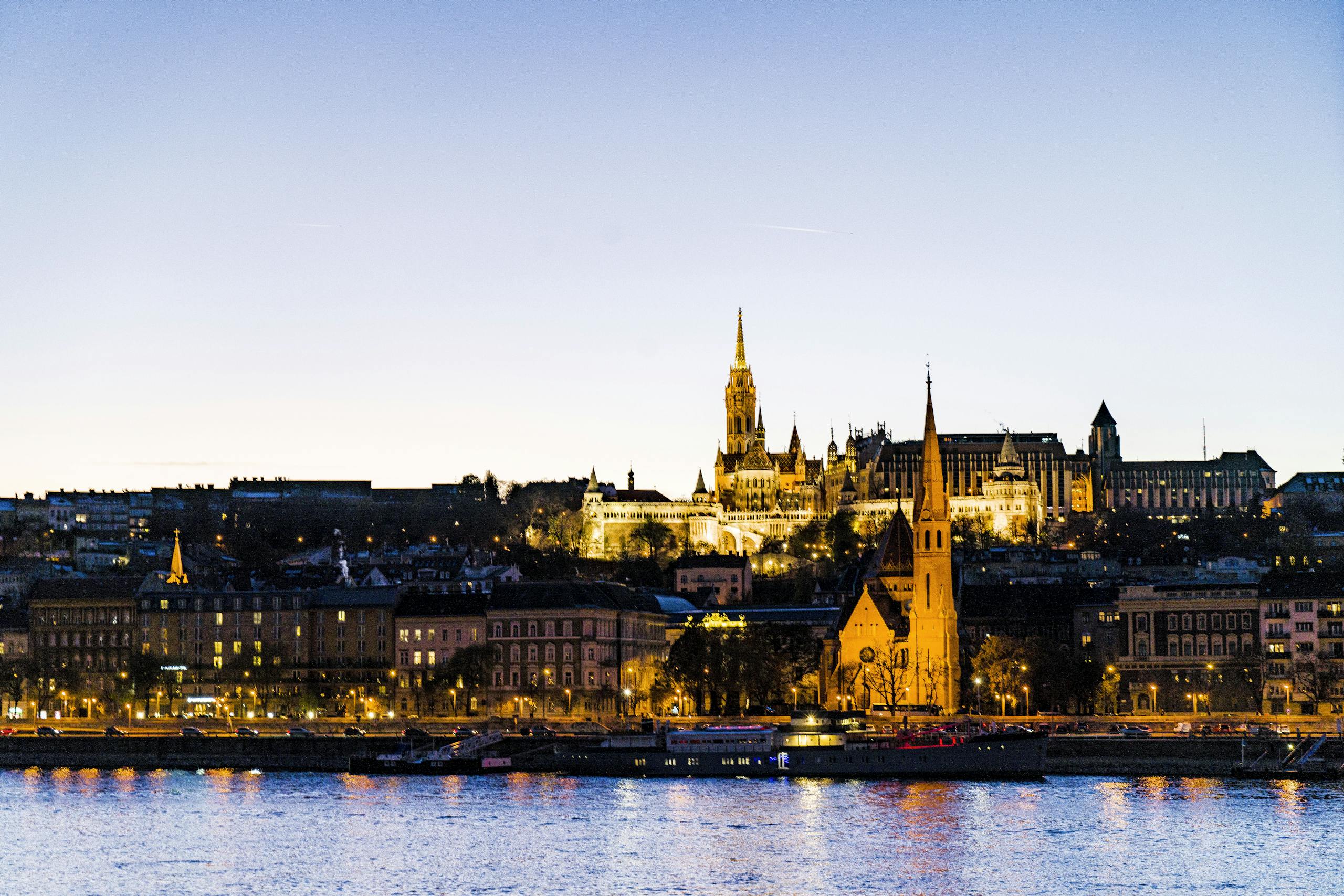 Scenic nighttime view of Budapest landmarks and Danube River reflecting lights in twilight.