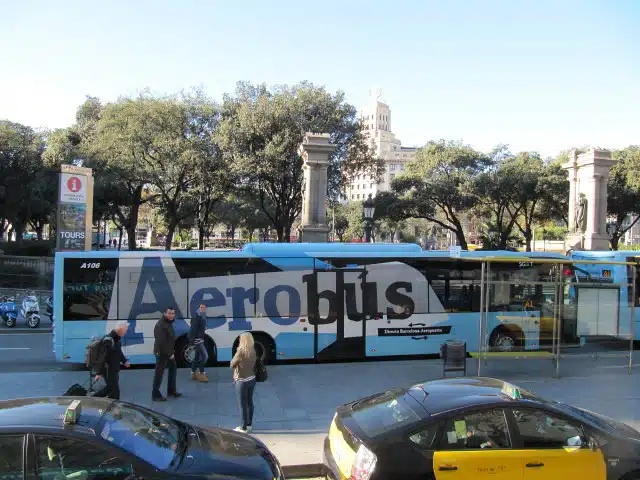 Blue and white Aerobús at a city stop with text reading Directe Barcelona-Aeroport