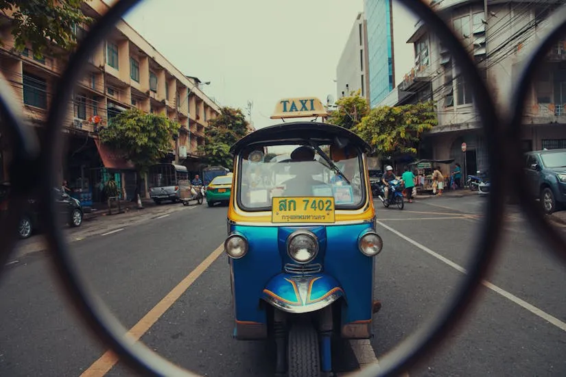 A colorful tuk-tuk on a busy urban street surrounded by city life and architecture.