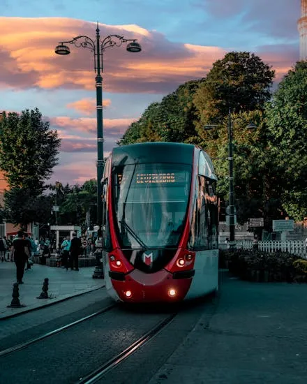 A vibrant tram navigating through a city street at sunset with beautiful sky.