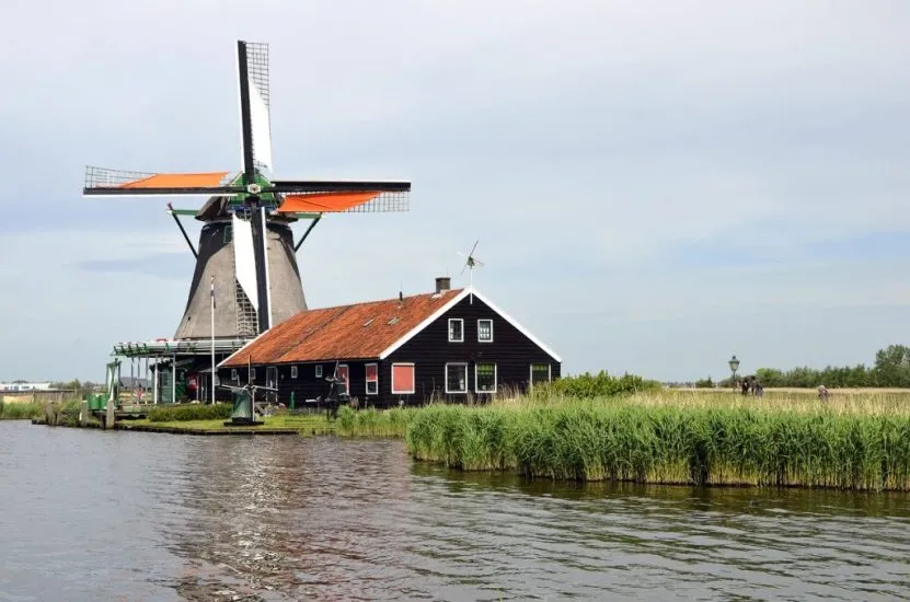 Traditional Dutch windmill with orange sails and a dark wooden house beside a canal in the Netherlands