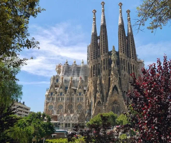The intricate facade and towering spires of the Sagrada Família basilica in Barcelona, framed by trees