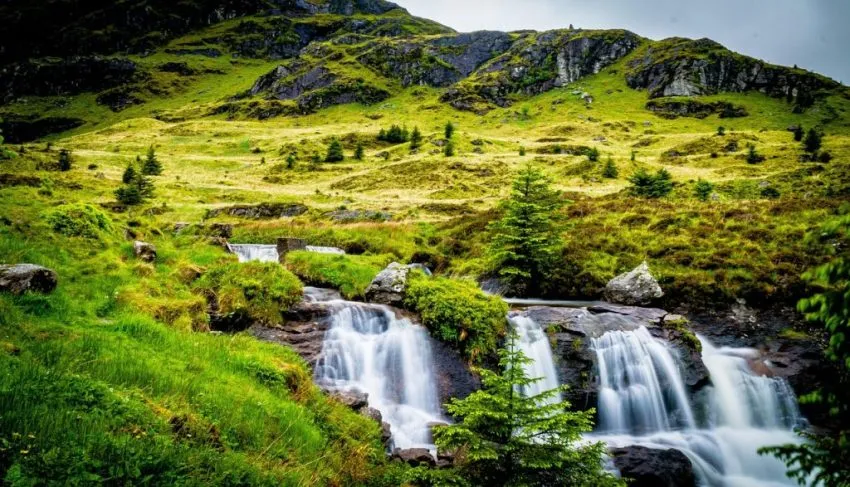 Waterfall cascading over dark rocks on a lush green hillside with rocky outcrops in the Scottish Highlands