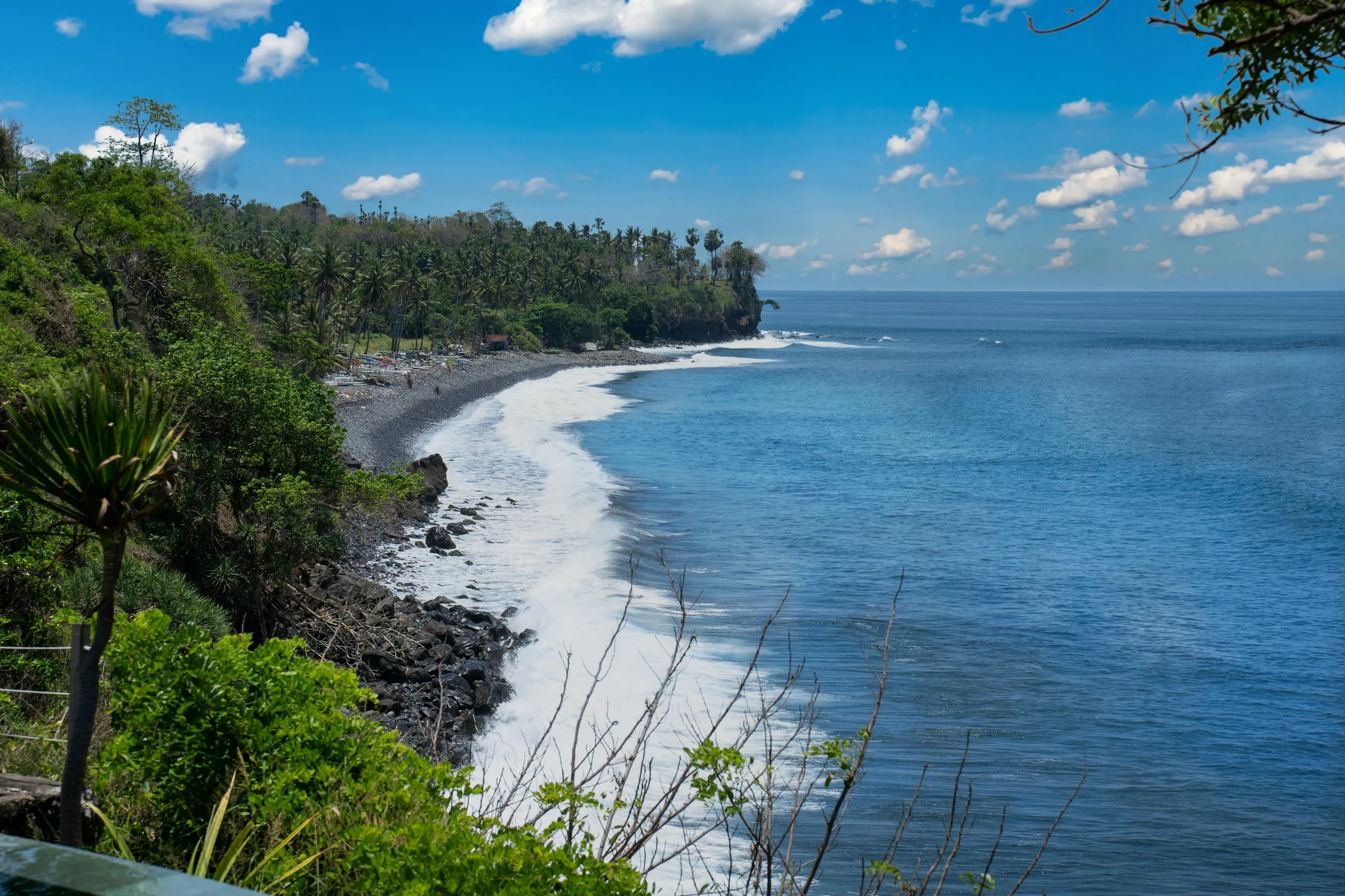 Serene view of Bali's rocky coastline with lush greenery and blue ocean under a vibrant sky.