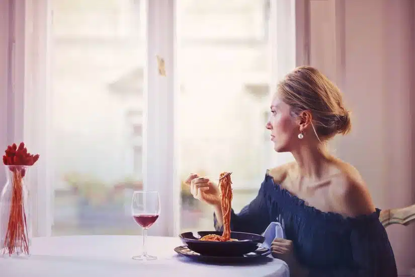 A woman enjoying a meal of spaghetti and wine at a restaurant table, elegantly dressed.