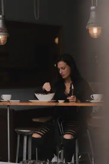A woman enjoys a meal at a restaurant table with moody lighting, creating a relaxed atmosphere.