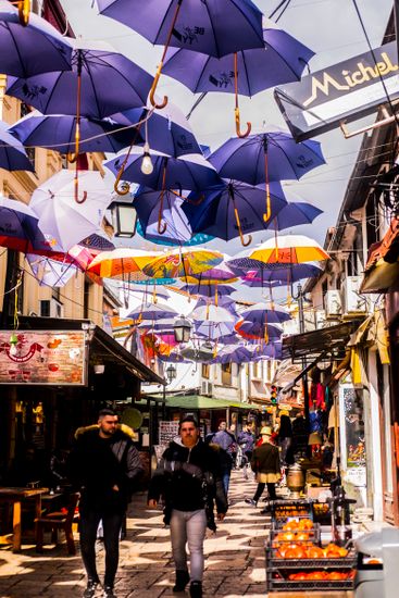 Stylish men strolling on narrow street between buildings under bright umbrellas in town
