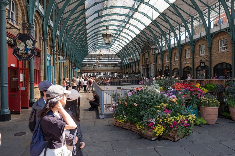 Vibrant flowers in London's iconic Covent Garden Market, busy with tourists and locals enjoying a sunny day.